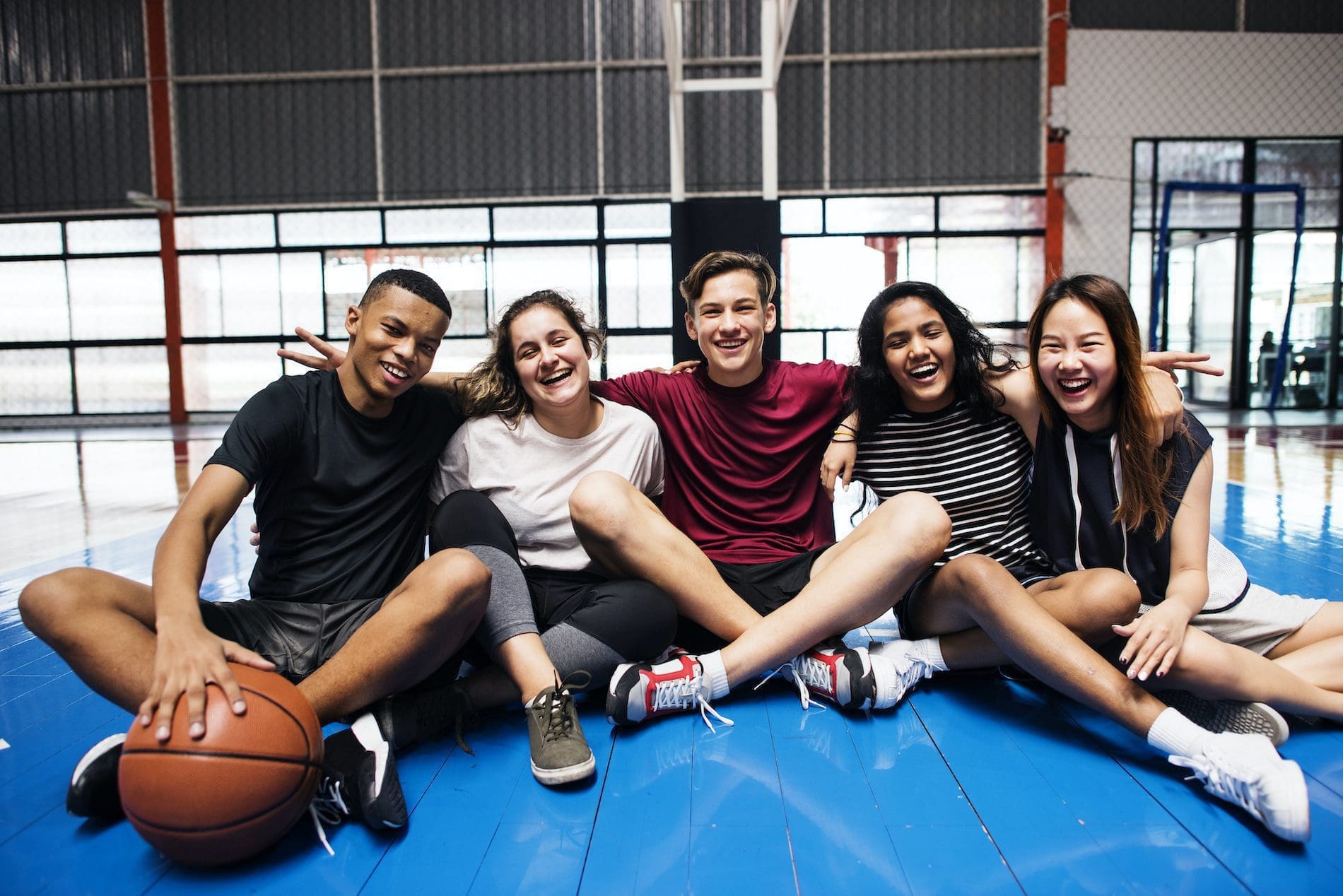 Students sitting and smiling on a gym mat.