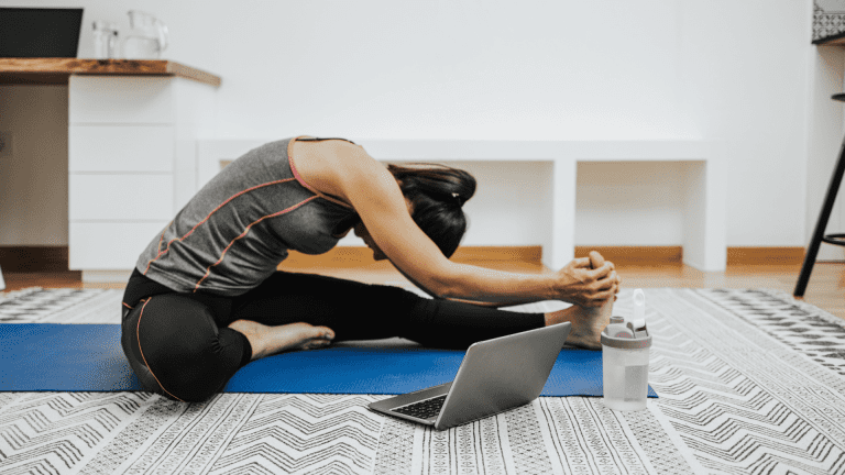 A person stretches at home next to laptop.