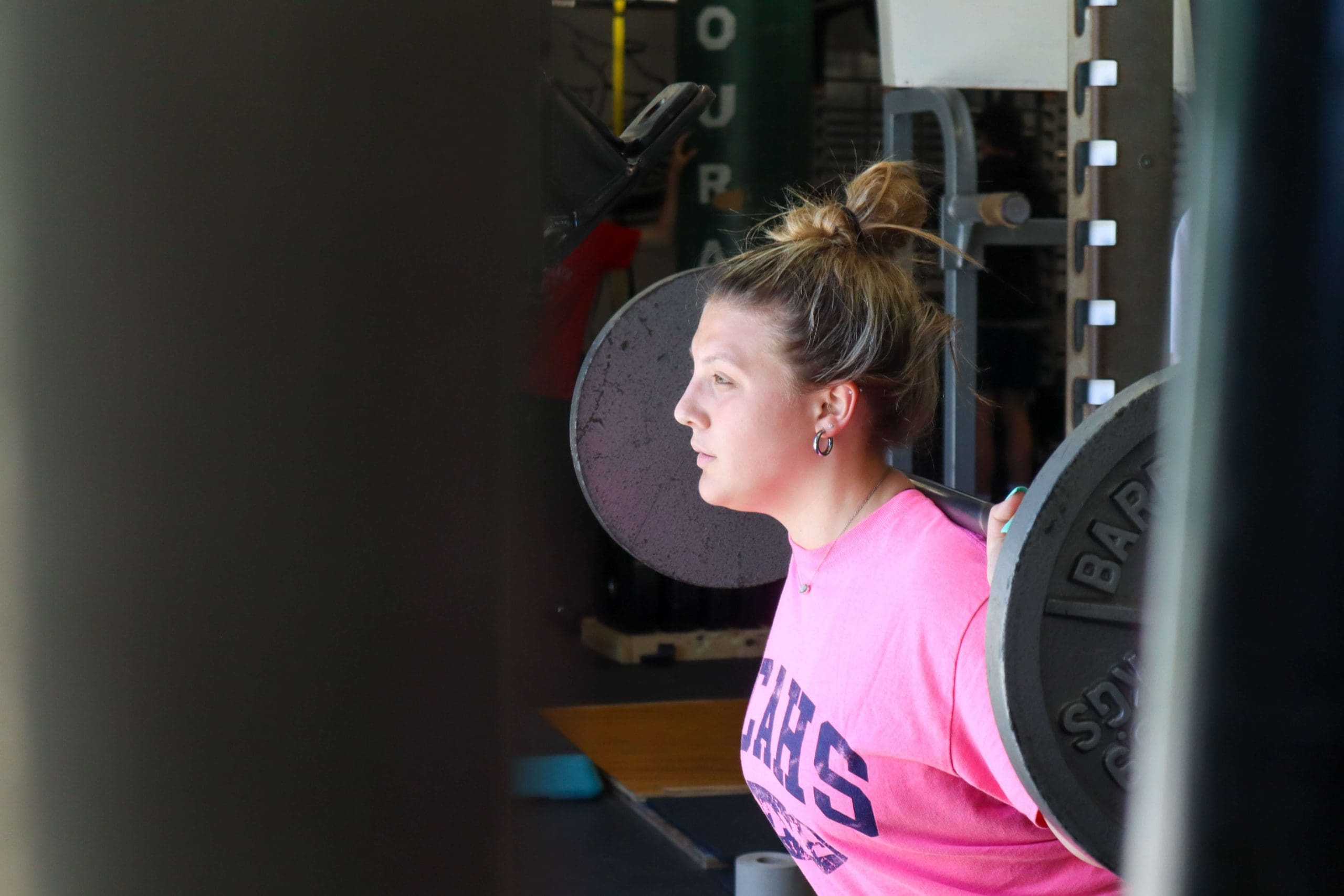A student performs a barbell back squat in physical education class.