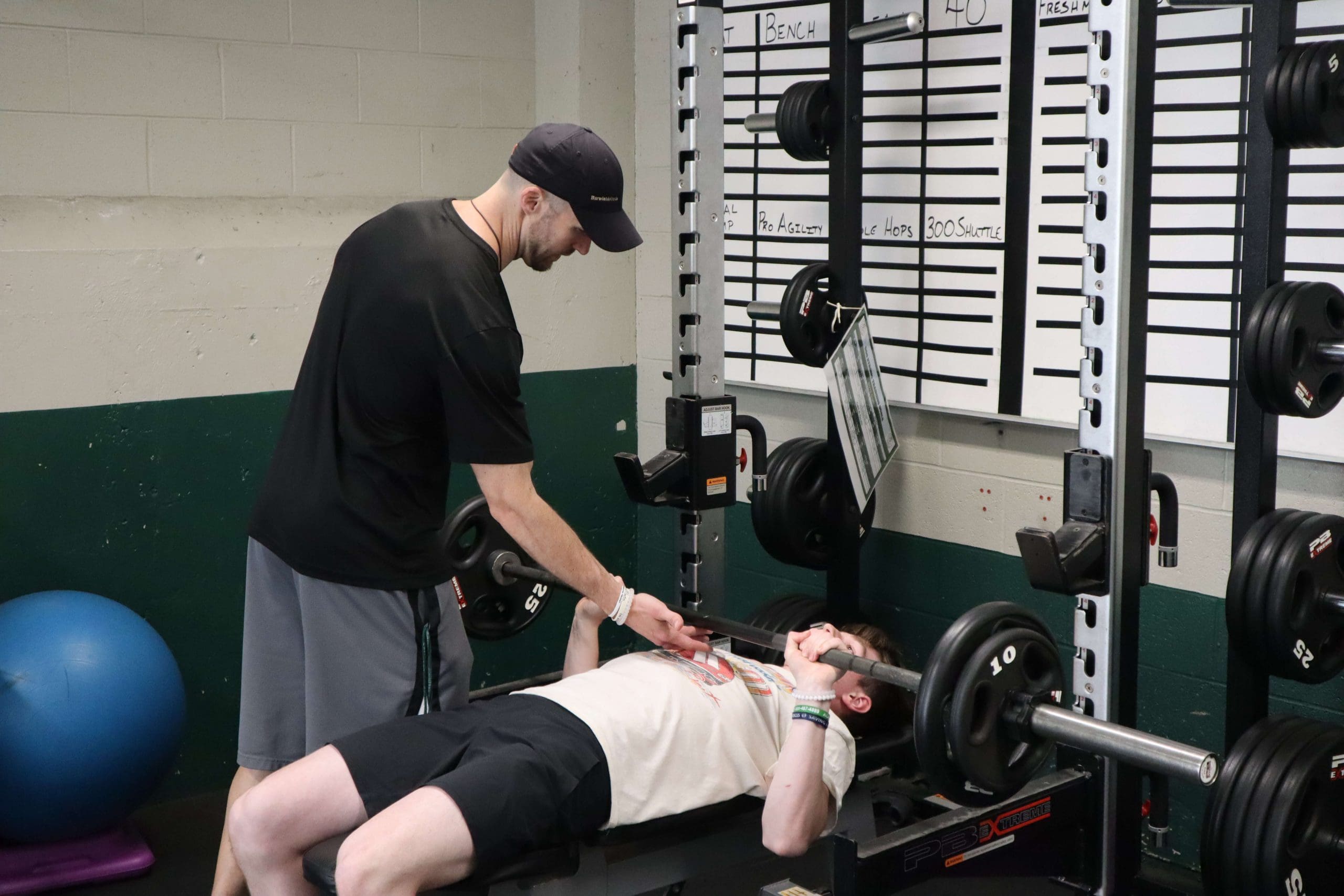 A coach instructs a student performing the bench press.