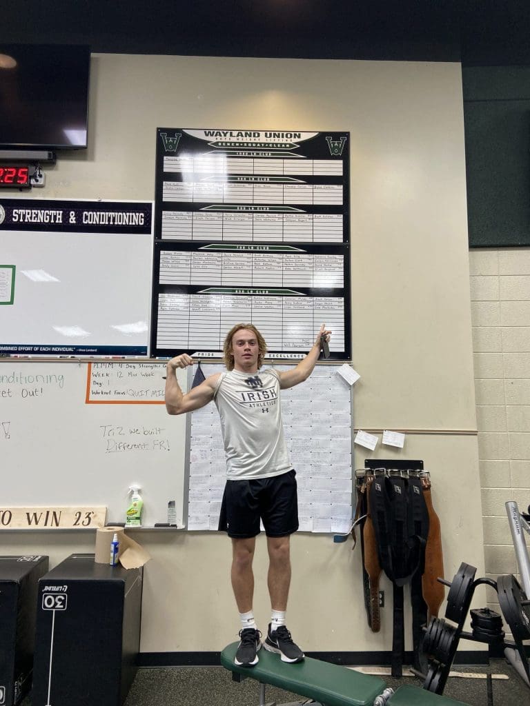 A student points at a leaderboard in a strength and conditioning class.