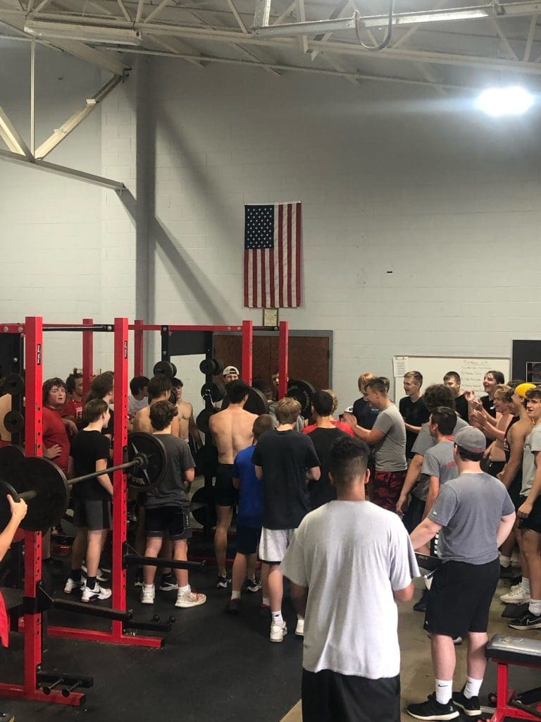 Van Wert football student athletes cheer on a teammate performing a weight lifting movement.