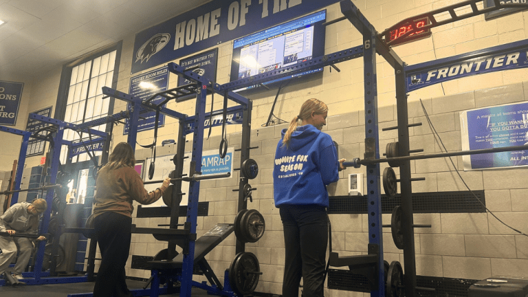 Frontier High School students working out in the weight room with PLT4M displayed on TV.