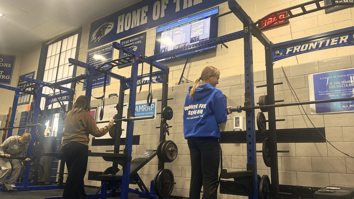 Frontier High School students working out in the weight room with PLT4M displayed on TV.