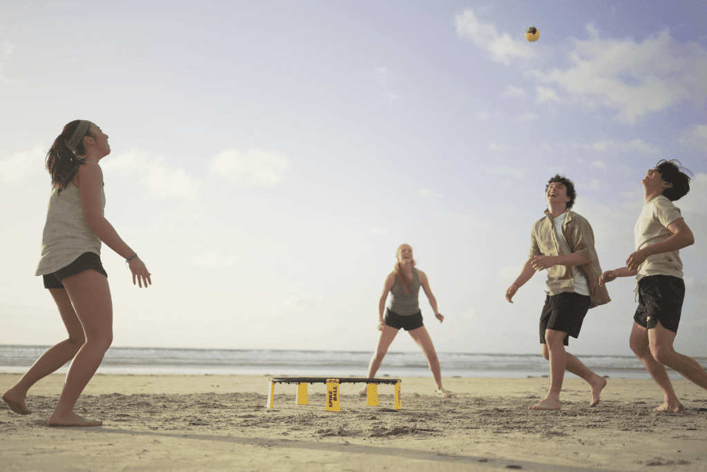 Teenagers playing Roundnet with Spikeball equipment on a beach.